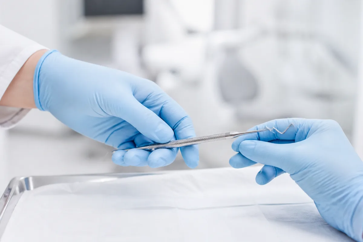 Mains gantées manipulant un instrument fin au-dessus d&rsquo;un plateau stérile, arrière-plan flou et lumineux